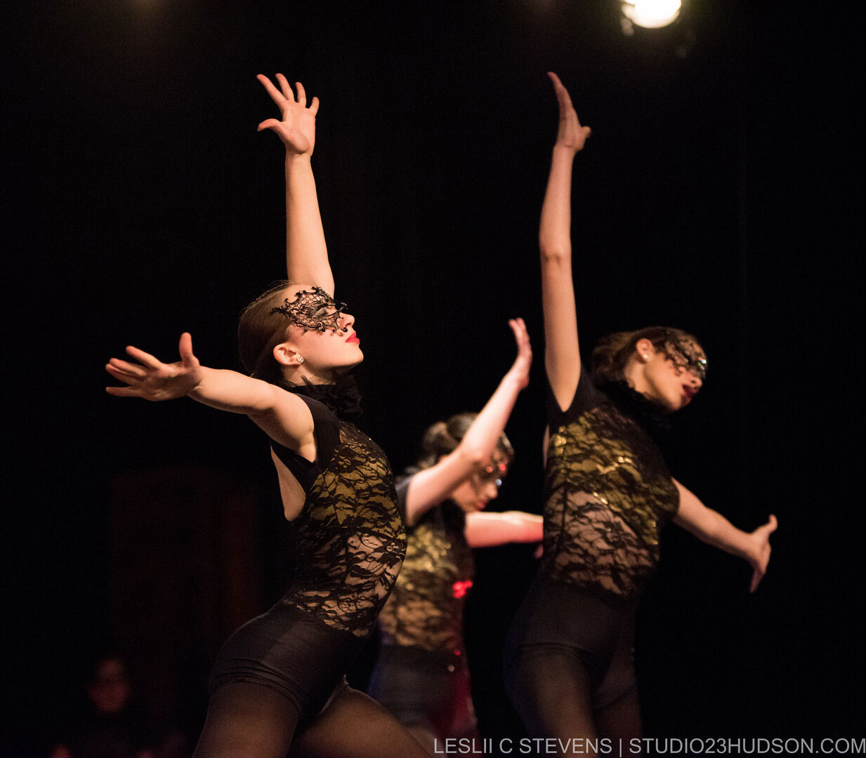 Three dancers in black and gold costumes performing with arms raised.