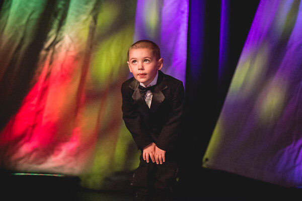 A young boy in a suit posing against a colorful backdrop.