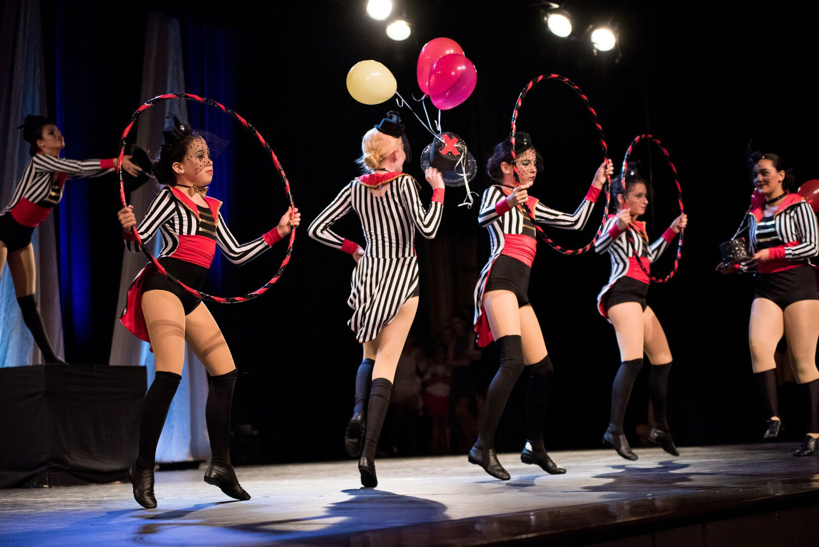 Four female dancers performing with red hoops on stage.