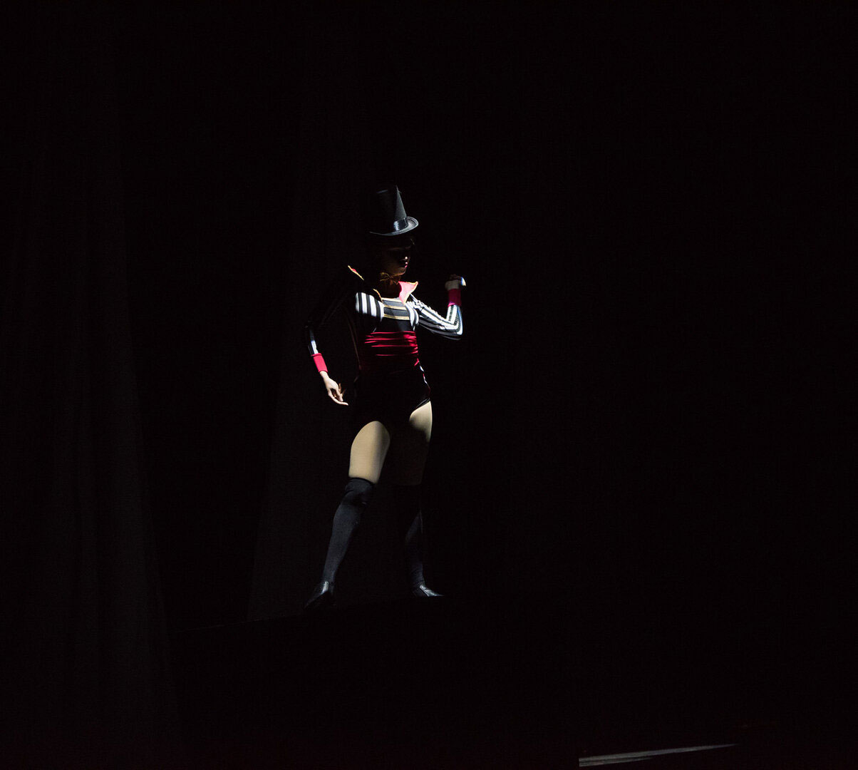 A person in a dark outfit illuminated against a black background.