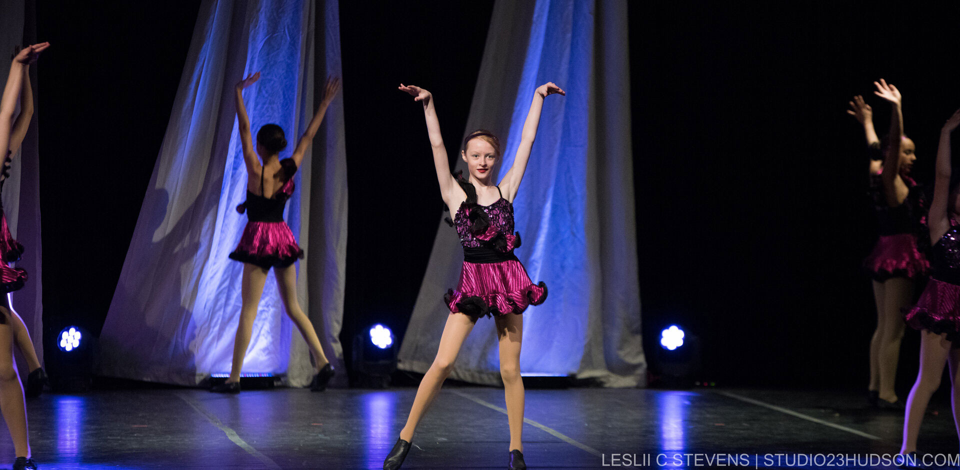 Young ballerinas performing on stage in purple and black costumes.