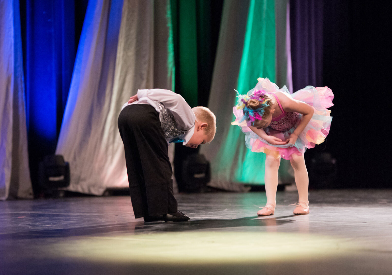 Two children bowing on stage, holding flowers.