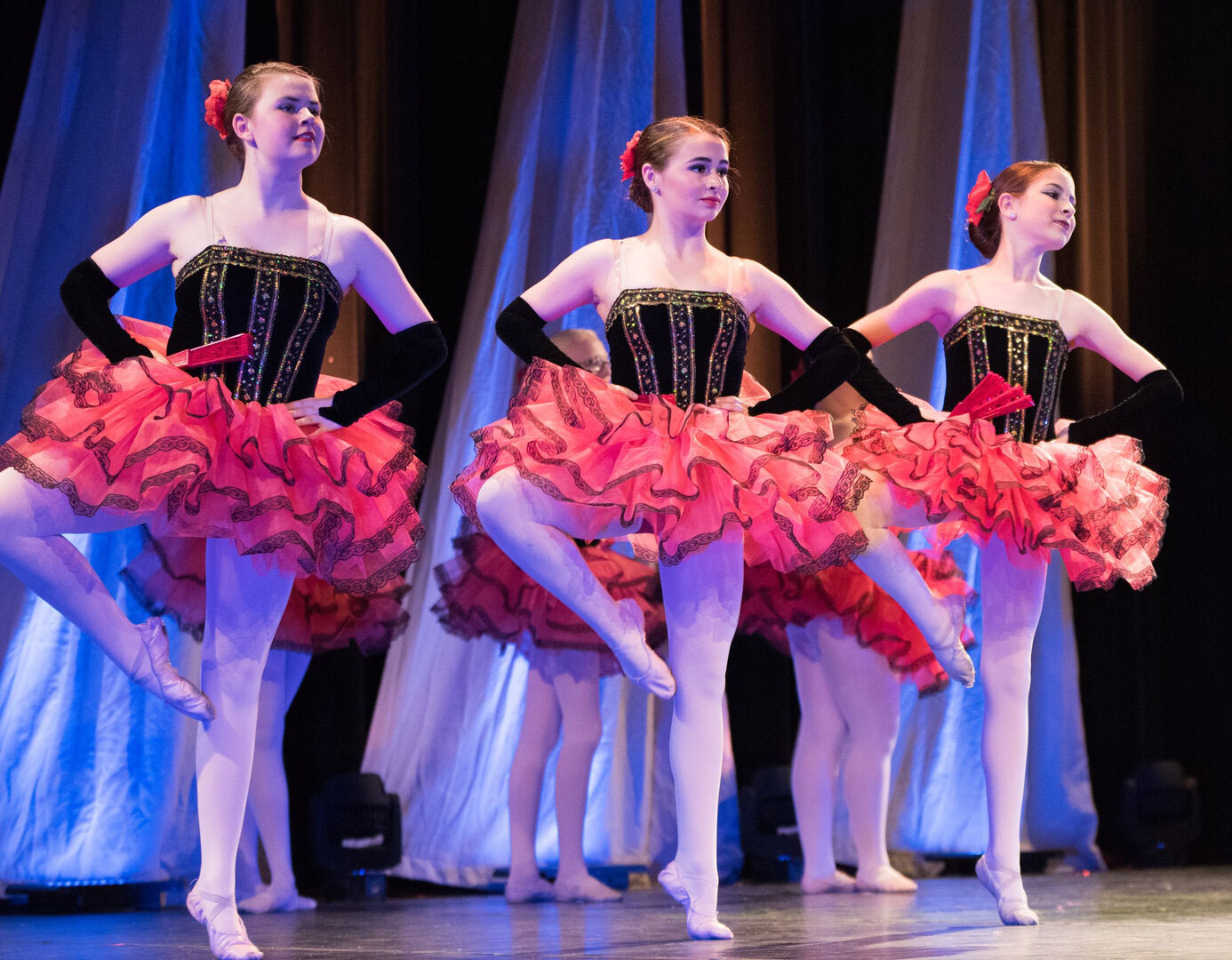 Three ballerinas performing on stage in black and pink costumes.