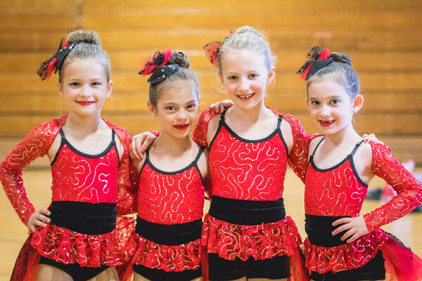 Four young girls in red dance costumes posing together.